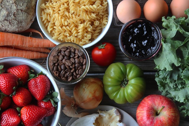 Fresh pasta, coffee beans, fruits and vegetables laid out on a wooden table.