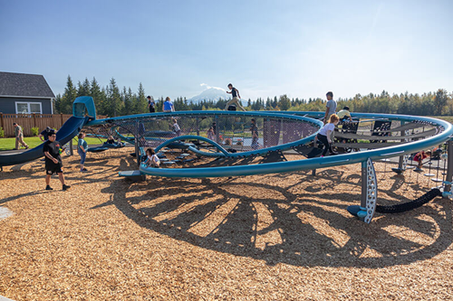 Children run and play on an infinity shaped playground with Mt. Rainier in the distant background.