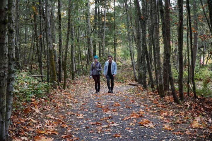 Couple walking hand-in-hand on Tehaleh nature trail through forest.