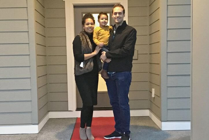 Young couple holding their toddler in front of their purchased home in Tehaleh.