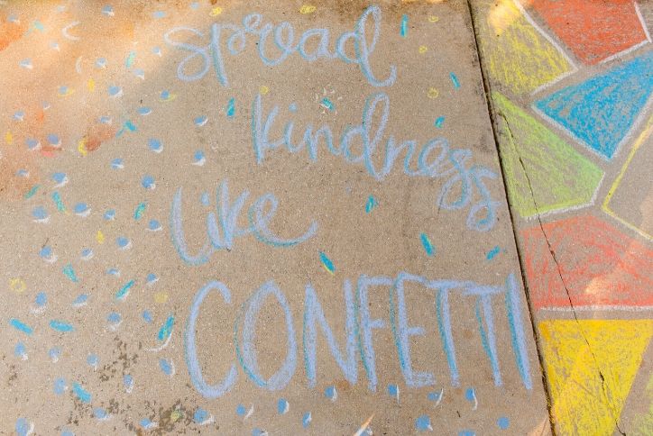 Spread kindness like confetti chalk writing on street.