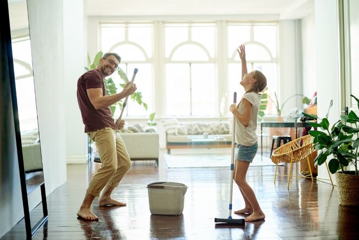 Father and daughter singing and dancing while cleaning wooden floor.