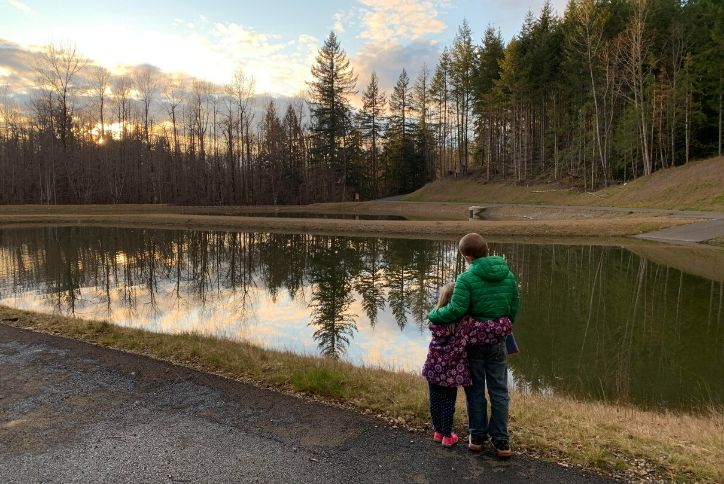 Young siblings holding each other while looking out on pond in Tehaleh.