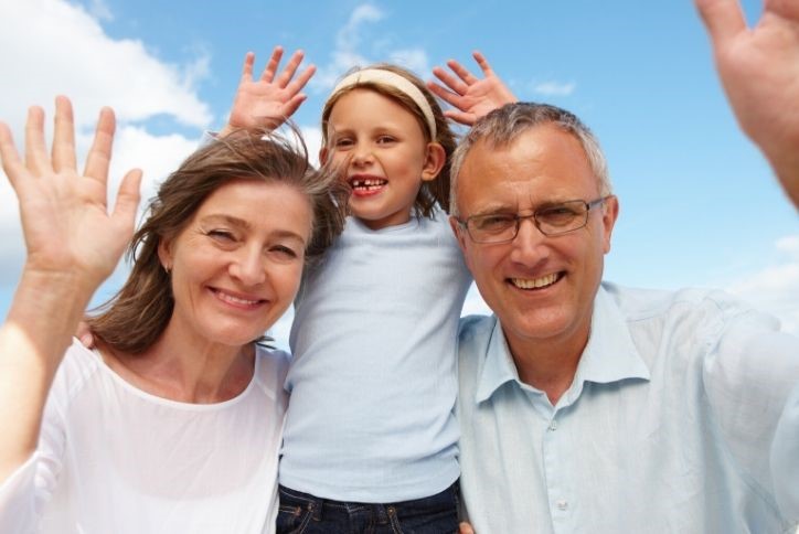 Parents and young daughter smiling and waving with sky blue background.